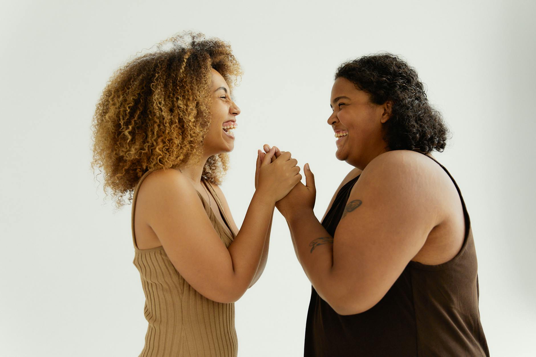 women in beige and brown tank top holding hands while looking at each other